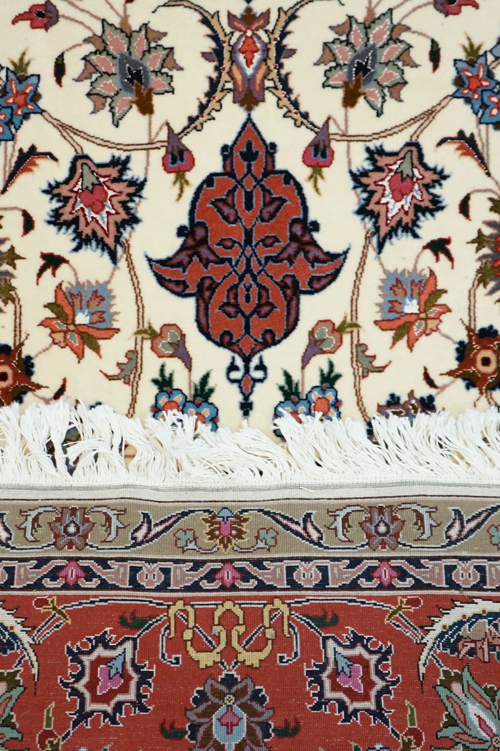 Close detail of a hand-knotted rug, its floral motifs worked in cream, coral and indigo